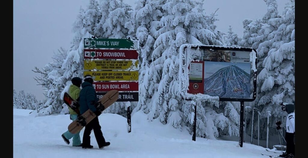 Snowboarders at Stratton Mountain trail signs on a snowy winter day